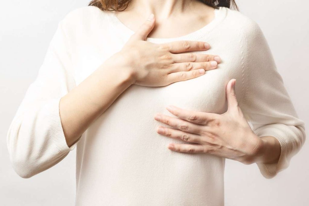mulher palpa a mama buscando sintomas de câncer de mama